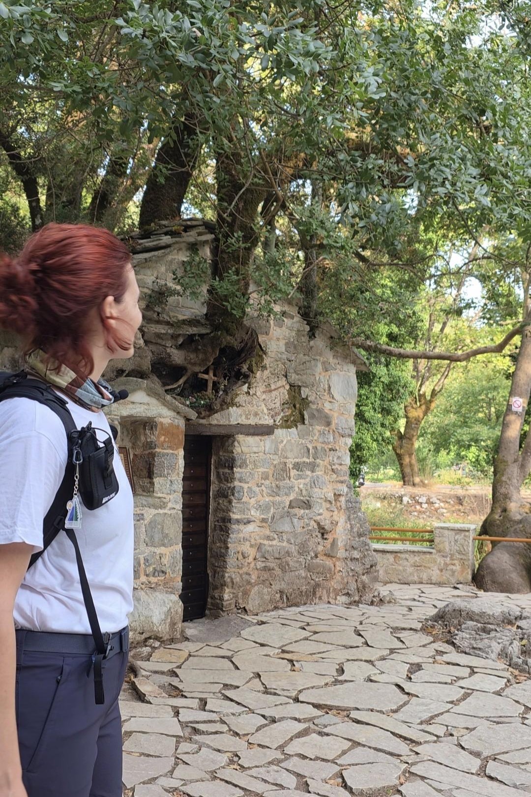 Επισκέπτρια μπροστά στο πέτρινο εκκλησάκι της Αγίας Θεοδώρας στη Βάστα Αρκαδίας, κάτω από τα μεγάλα δέντρα
